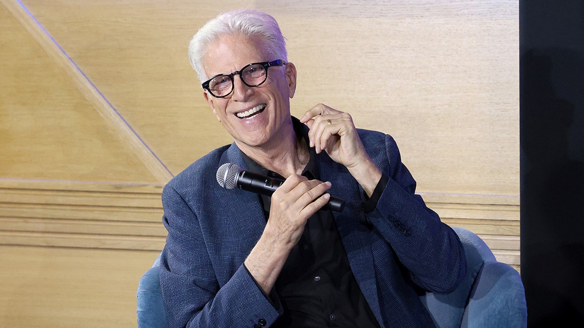 Ted Danson memegang mikrofon dan tertawa