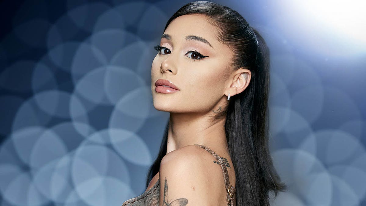 Ariana Grande memiringkan kepalanya ke belakang dan menatap kamera dengan gaya rambut setengah ke atas.