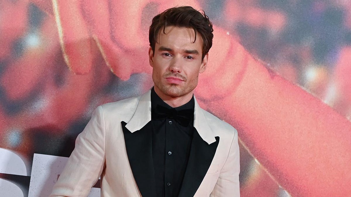 Liam Payne berdiri di karpet London dengan jaket putih berlabel hitam dan kemeja hitam