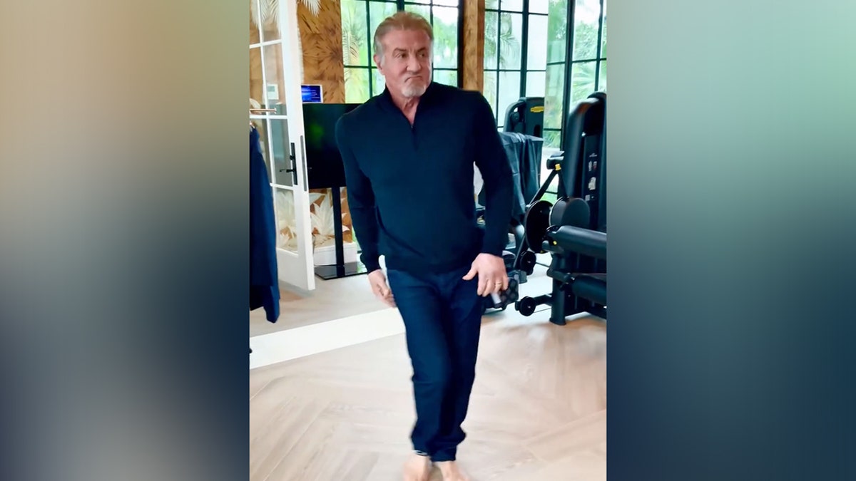 Sylvester Stallone dengan kemeja biru dan celana biru menari sambil mengenakan pakaian