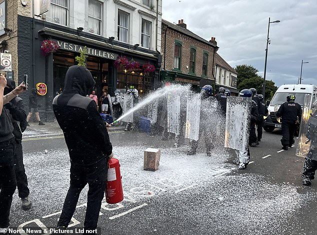 Para pengunjuk rasa melemparkan alat pemadam kebakaran ke arah petugas polisi anti huru hara saat terjadi kerusuhan di Sunderland pada 2 Agustus