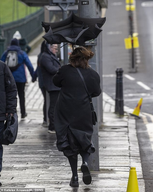 Seorang wanita memegang payungnya di Edinburgh saat kota itu menghadapi cuaca basah dan berangin