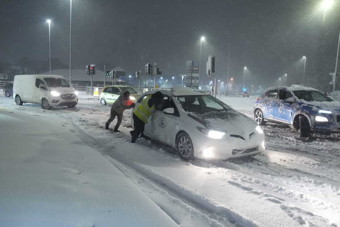 Orang-orang membantu mendorong mobil yang terjebak salju di Leeds, Inggris, Minggu, 5 Januari 2025.