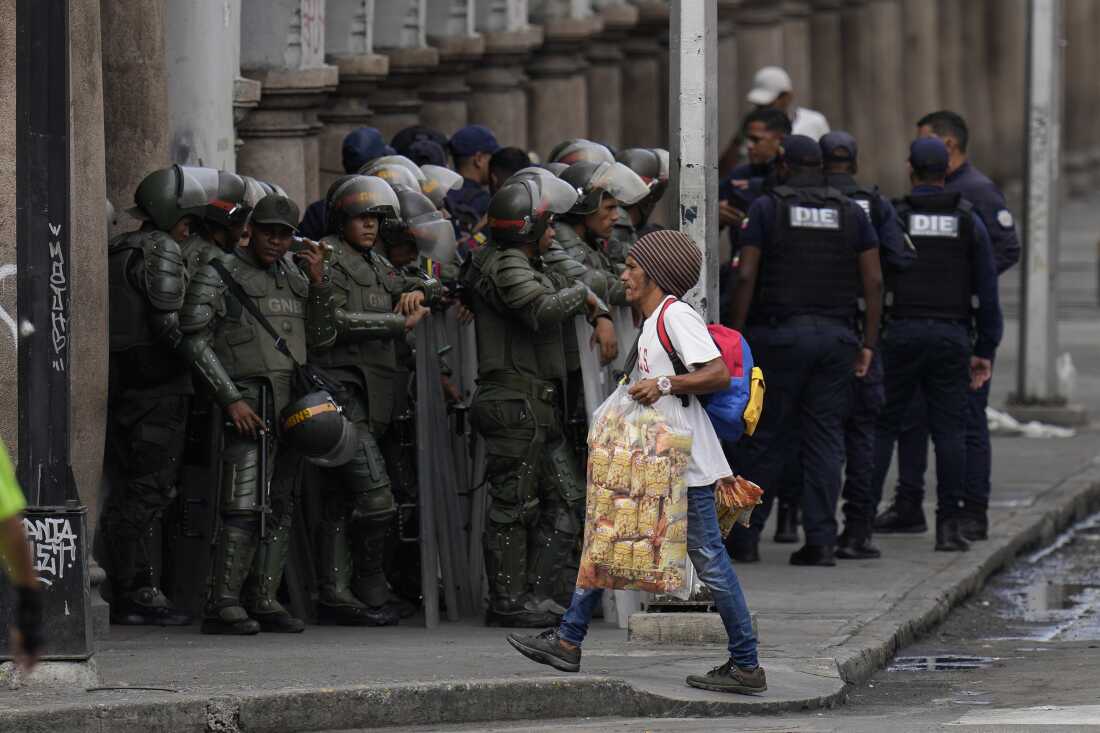 Seorang pedagang kaki lima berjalan oleh anggota Garda Nasional Bolivarian sebelum Presiden Nicolás Maduro dilantik untuk masa jabatan ketiga di Caracas, Venezuela