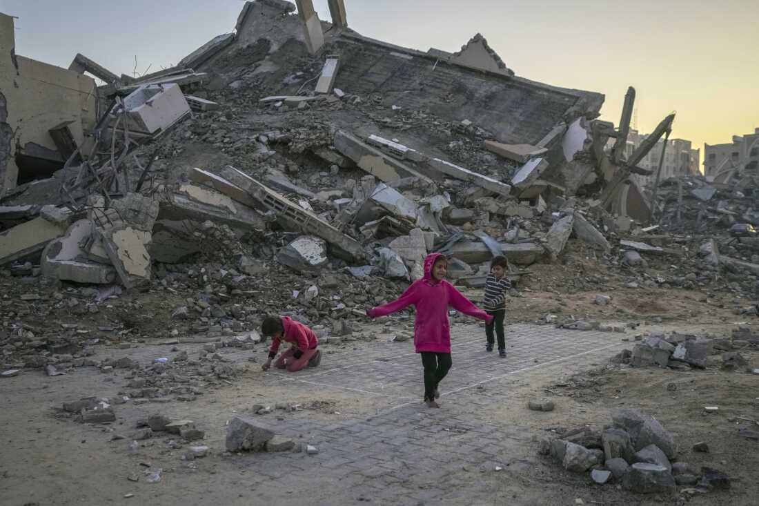 Anak-anak Palestina bermain di samping sebuah bangunan yang hancur akibat serangan Israel di kota Khan Yunis di Jalur Gaza tengah pada 1 Januari.