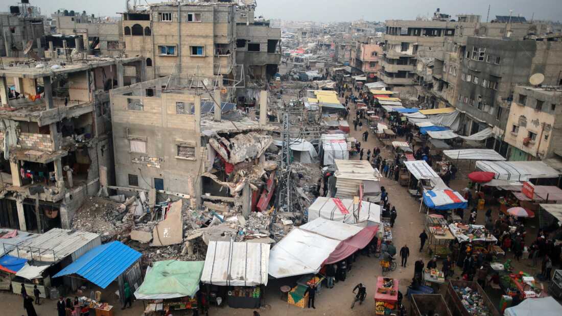 Orang-orang berjalan melewati kios-kios yang menjual barang di tengah puing-puing bangunan yang hancur akibat serangan Israel sebelumnya di Khan Yunis, Jalur Gaza selatan, pada 15 Januari 2025.